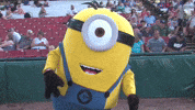 Sports gif. A person in a giant Minions mascot costume dances for us on the field as a baseball game, its arms flailing out to the side.