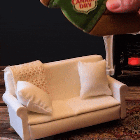 Sponsored gif. A hand places a lounging gingerbread man wearing a Canada Dry sweater onto a miniature couch. Text: "INTERNAL SLEIGHBELLS INTENSIFY"