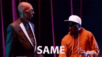TV gif. A man wearing a black suit points at himself and looks at us as he puts his hand on the shoulder of a man sipping champagne and wearing a hoodie and a baseball hat, who seems uninterested. Text, "same."