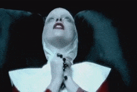 Music video gif. Lady Gaga in Alejandro is dressed as a nun. She holds a rosary in her hands as she lays on a black leather couch. She thrusts her hands in the air and says, "Alejandro," before bringing the rosary back to her lips.