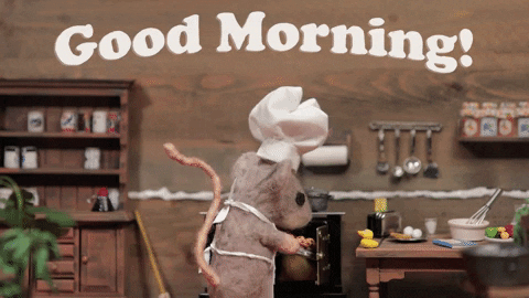 Cartoon gif. Stop motion brown felt mouse wearing a chef's hat and an apron pulls a tray of muffins out of the wood stove, tilting is head back as it takes in the aroma of the freshly baked muffins. Text, "Good morning." 