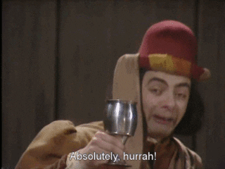 TV gif. Mr. Bean dressed in a medieval costume and blunt bob hairdo, holds a silver chalice up to toast. With an awkward, wide grin, he cheers, “absolutely, hurrah!”