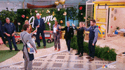 Reality TV gif. A man applauses in congratulations as a group of people on the show Making It, hold up champagne glasses in a toast.
