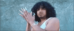 Music Video gif. Scene in Rosalia’s Haute Culture music video. Man looks down at us with a serious expression as he claps hands that have ornately decorated long nails.