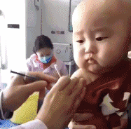 Video gif. A doctor gives a baby a shot in the arm, and once it's done the baby strains its face like its about to cry.