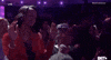 Video gif. Black women stand in a large crowd, swaying to music. They hold their hands up in praise.