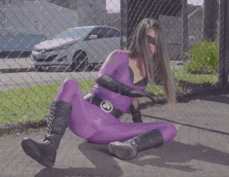 Video gif. A woman in a superhero spandex suit and black mask sits on the ground with her knees spread and starts clenching with all of her strength. Some kind of bright purple power comes forms in her crotch and we zoom in to see her face as she screams powerfully.