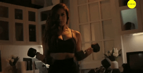 Music video gif. A scene from Big Bang Music where a woman in dressed in athletic clothes and lifts two dumbbells. 