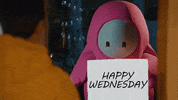 Video game gif. A pink character with a white face blinks its black eyes as it holds a sign that reads, "Happy Wednesday."