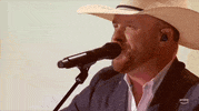 Academy of Country Music Awards gif. Cody Johnson sings into standing mic, smiling with his eyes he has a positive demanor as he refocuses from glancing out into the distance to in front of him.