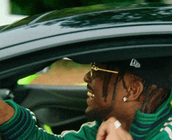 Celebrity gif. BRS Kash is driving in his car and looks very happy as he cruises down the street, bopping along to the music.