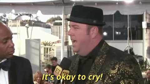 Celebrity gif. At the Golden Globes, Chris Sullivan wears a black top hat and gold suit and smiling says, “It’s okay to cry!”