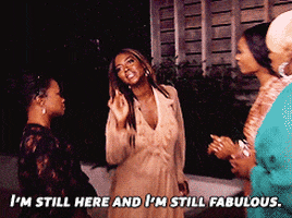 Reality TV gif. Kenya Moore from Real Housewives of Atlanta is wearing a peach dress and she points at the ladies with confidence, saying, "I'm still here and I'm still fabulous."
