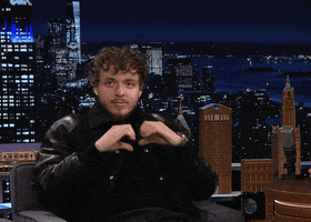 Celebrity gif. Jack Harlow on The Tonight Show Starring Jimmy Fallon makes a heart with his hands at the audience. 