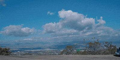 Movie gif. Fifties-style blue car drives slowly and parks in front of a mountain background in the movie A Glimpse Inside the Mind of Charles Swan III. There are two sunny-side up egg decals on the side of the car.