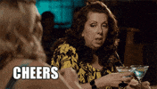 TV gif. Bette MacDonald as Trudy in Mr. D. She raises two martini glasses in both hands and clinks herself as she says, "Cheers."