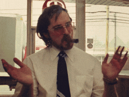Movie gif. Christian Bale as Irving Rosenfeld in American Hustle has a large cigar in his mouth and he claps while looking around the room.