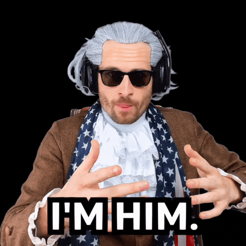 Video gif. A man wearing a cheap powdered wig, wayfarer sunglasses, red, white, and blue scarf, and white jabot points at himself, raises an eyebrow, and says "I'm him," which appears as text.