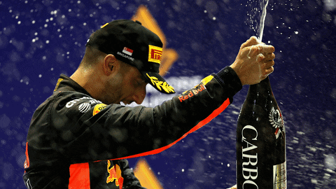 Sports gif. Daniel Ricciardo holds a giant bottle and joyfully sprays champagne everywhere.