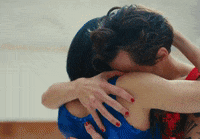 Music video gif. From the As it Was video: Looking sad and concerned, a tattooed Harry Styles hugs a woman, then pulls away, locking eyes with her in a moment of emotional intimacy.