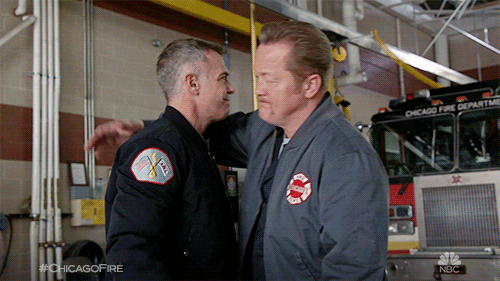 TV gif. Christian Stolte as Mouch and David Eigenberg as Christopher on Chicago Fire hug and pat each other on the back in a Fire Station. Then they firmly shake hands and smile at each other with appreciation.