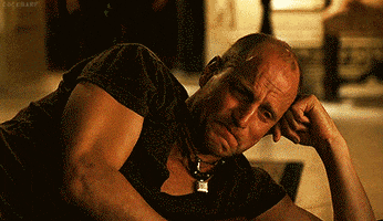 Movie gif. Woody Harrelson as Tallahassee in Zombieland lays on the ground, on his side, using his arm to prop his head up. He cries and picks up a stack of cash, using the hundred dollar bills to soak up his tears.