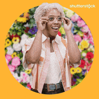 Sponsored gif. Woman takes off her glasses and looks around with a wide-eye expression of wonder on her face. The background behind her is all flowers. Text reads, “Beautiful.”
