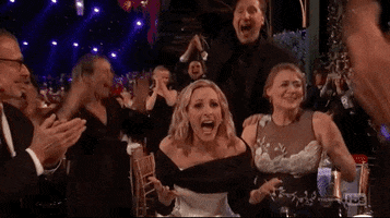 Celebrity gif. Marlee Matlin at the sag awards opens her mouth in shock and places her hands near her temples as people clap and celebrate around her. 
