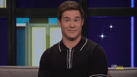 Celebrity gif. Adam Devine on Little Late with Lilly Singh smirks, then tilts his head to the side as he blinks rapidly.