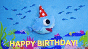 Digital illustration gif. Baby Shark stuffie swims across the bottom of the ocean floor wearing a red and white polka dot birthday hat that slides on and off its head. He's edited to look like his fins are moving as he bobs up and down in the water, giving the appearance of swimming. Fish pass by and bubbles emerge from the bottom. Text, "Happy Birthday!'