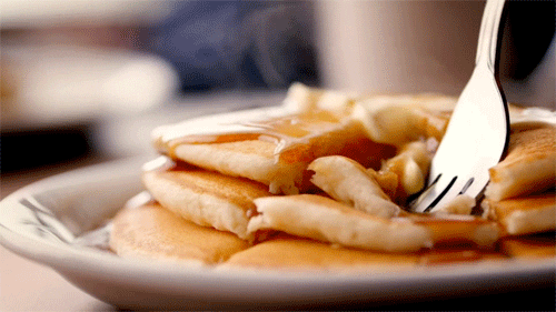 Video gif. Hot plate of steaming pancakes and syrup is cut into with a fork and looks scrumptious.