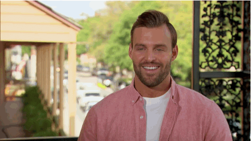 Reality TV. Robby Hayes on The Bachelorette has a big smile on his face and holds up his crossed fingers on both hands. He laughs and says, “Fingers crossed!”