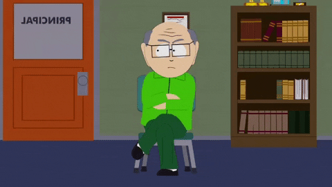 Cartoon gif. Mr. Garrison on South Park sits with his legs and arms crossed with an angry look on his face as he sits in the principal’s office.