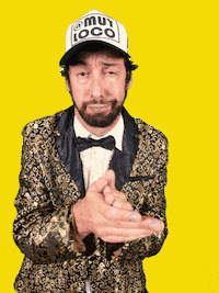 Video gif. Against a flashing yellow background, wearing a trucker hat and a shiny gold jacket, a bored-looking man with a beard claps at us.