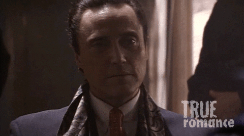 Movie gif. Christopher Walken as Vincenzo Coccotti in True Romance looks over his shoulder and then swings back around with a smug smirk on his face.