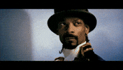 Music video gif. Snoop Dog in Welcome to the World of Plastic Beach, wearing a black top hat and regency naval attire nods seriously looking off into the distance. 