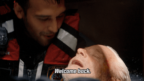 TV gif. Ryan Guzman as Eddie Diaz on 911 is wet and wears a safety vest as he holds an older man in his arms. Eddie and the older man smile at each other in happiness as Eddie says, “Welcome back.”