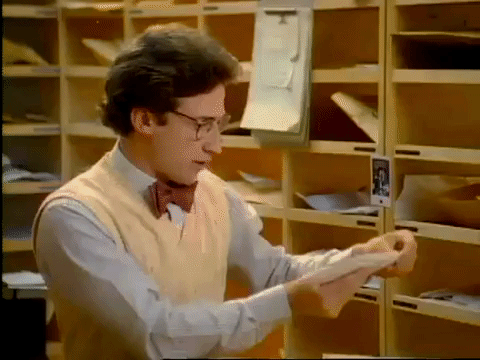 TV gif. A scene from Soul Train. A man in a mailroom slides mail into cubby holes while chewing gum. He claps his hands once he’s done with that stack of letters and he happily picks up another stack. 
