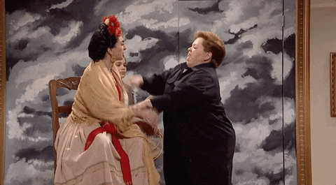 SNL gif. Melissa McCarthy dressed as a repairwoman gets into a swatting fit with a Frida Kahlo impersonator in front of a large black-and-white painting of a cloudy sky.