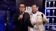 TV gif. On the interview stage at the 2024 ACM Awards, singer and rapper Jelly Roll and the interviewer are both shrugging towards the camera.