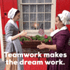 Video gif. Two women dressed in colonial-style clothes do a fist bump handshake. Text, "Teamwork makes the dream work."