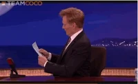 Celebrity gif. Talk show host Conan O'Brien looks up from a sheet of paper and pretends like he's shocked to see us. He turns to face us and sets the paper down, saying, 