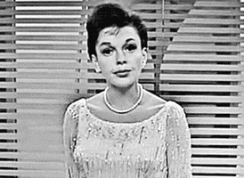 Celebrity gif. Judy Garland wears a shimmering dress and a pearl necklace as she tilts her head and stares at us with a thoughtful expression, as if she's genuinely considering something.