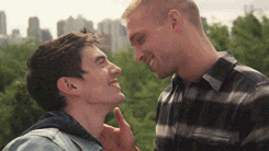 Music video gif. Steve Grand in the video for Stay kisses a man in various idyllic scenes around a city, in a park, and near a waterfront.