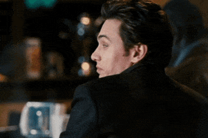 Movie gif. James Franco looks over his shoulder at us, then grins and winks.