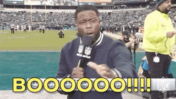 Celebrity gif. Kevin Hart stands on the sidelines of a football field with a mic in his hand. He turns to the crowd and raises his fist up, mockingly yelling, “Booooooo!!!!”