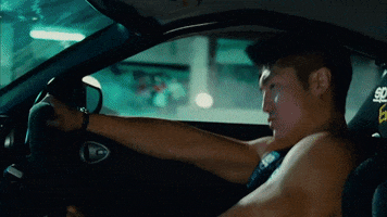 Movie gif. Brian Tee as DK in the Fast and the Furious Tokyo Drift sits behind a steering wheel as the black race car drifts sideways up a ramp. 