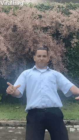 Video gif. Man poses awkwardly as we zoom out away from him. As he poses, almost frozen like a statue, a white dog jumps up and bites his crotch The man quickly grabs his groin in pain as the dog walks through his legs.