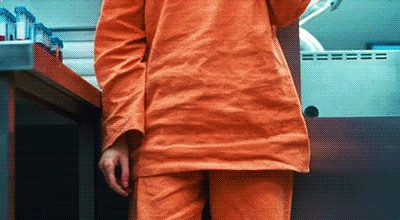 A white girl in orange dress sat on the floor holding a black gun.
