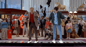 Movie gif. Tom Hanks as Josh and Robert Loggia as MacMillan in Big. Both men are dancing on a giant piano in a toy store with many onlookers, all impressed with their unison of dance and rhythm.  